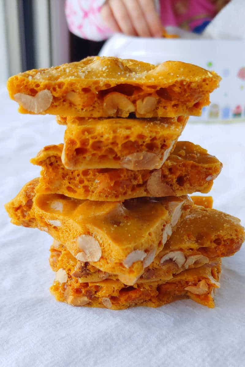 a stack of microwave peanut brittle, with a girl taking some from a tin in the background