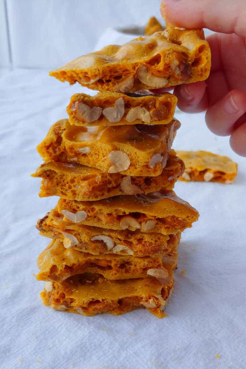 a stack of microwave peanut brittle, with a hand placing another piece on top
