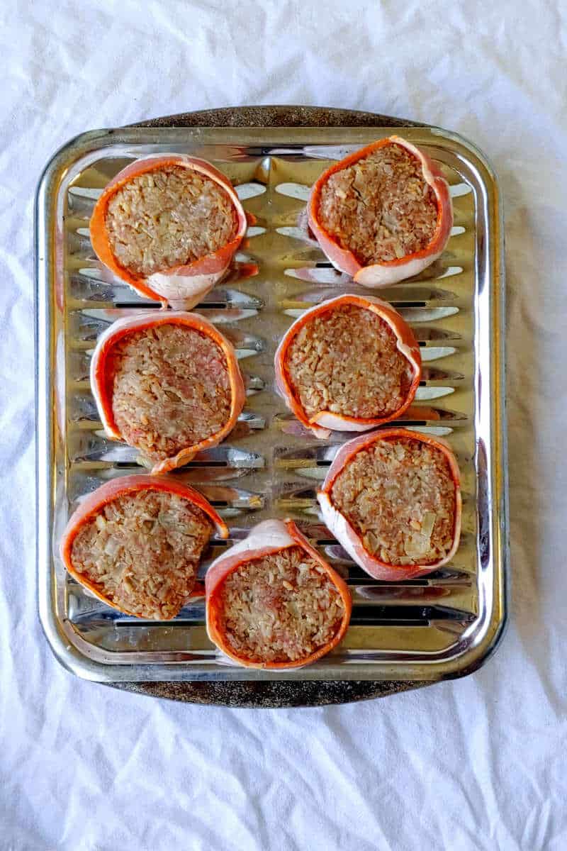 uncooked fake steak patties, wrapped in bacon, on a broiler pan tray